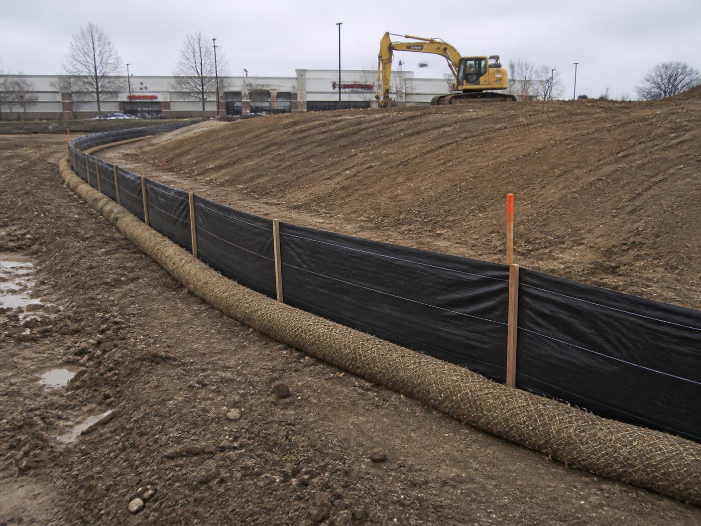Silt fence and compost filter sock installed along a graded slope on a commercial construction site
