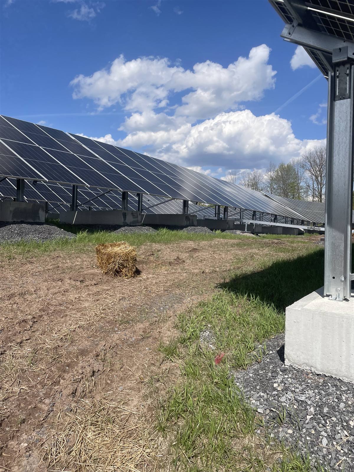 Solar array pier foundation beside straw-covered ground